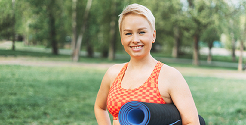 young woman with yoga mat in a park