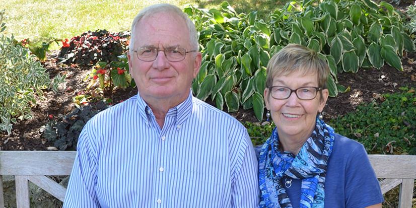 elderly couple smiling in front of a garden