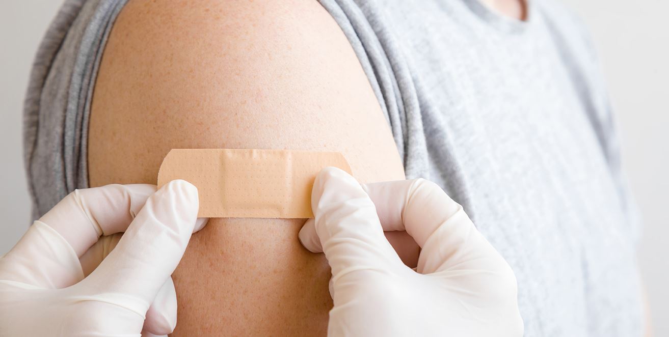 gloved hands placing a bandaid on an arm